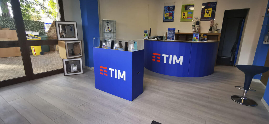 Comptoir en carton ORIZABA avec affiches et logos TIM intégrés, utilisé dans l’aménagement d’un espace commercial pour le service client, avec plateau de travail et vitrine transparente pour présentation des produits ou services - Le Meuble en Carton une marque du groupe Natur Design
