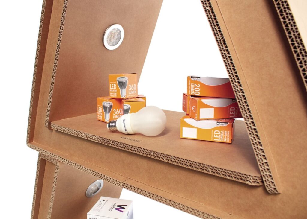 Présentoir en carton écologique pour stands événementiels et décoration de magasins, avec plateau en carton perforé supportant des boîtes de lumières LED 360 lumens et packs de produits professionnels (ex. : LED 200 lumens), idéal pour l’aménagement d’espaces commerciaux ou les salons professionnels - Le Meuble en Carton une marque du groupe Natur Design