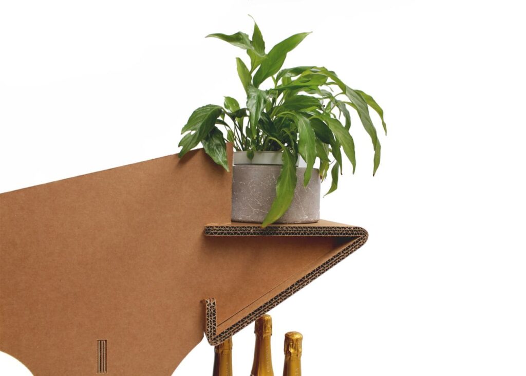 Présentoir en carton écologique PAGET pour stands événementiels ou décoration de magasins, avec plateau cartonné supportant une plante verte dans un pot et des bouteilles dorées en verre, idéal pour ambiance naturelle et professionnelle - Le Meuble en Carton une marque du groupe Natur Design